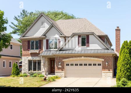 Une maison de banlieue en brique rouge et vinyle blanc avec un garage pour deux voitures, un sommet au-dessus de la porte d'entrée, et un aménagement bien entretenu. Banque D'Images
