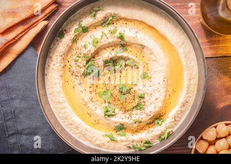 Cuisine arabe; trempette crémeuse traditionnelle de houmous dans un bol sombre. Recouvert d'huile d'olive, de paprika et de persil. Vue de dessus avec gros plan. Banque D'Images