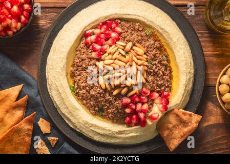 Cuisine arabe ; trempette crémeuse traditionnelle à l'houmous avec bœuf haché. Garnie d'huile d'olive, de graines de grenade fraîches, de pignons de pin rôtis et de persil. Banque D'Images