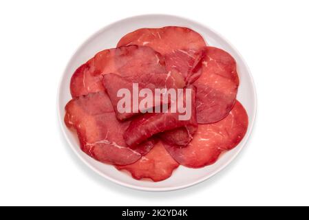 Tranches de bresaola dans une plaque blanche isolée sur un chemin de coupure blanc, salami de bœuf italien séché de Valtellina Banque D'Images