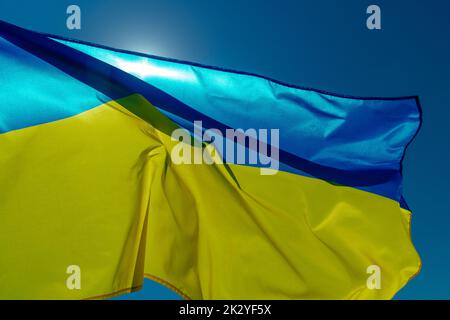 le drapeau ukrainien vole sur le ciel bleu par jour ensoleillé, rétroéclairé par le soleil Banque D'Images