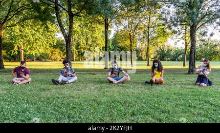 groupe d'amis multiraciaux assis dans un parc public à l'extérieur, utilisant des smartphones pour partager du contenu sur les réseaux sociaux Banque D'Images