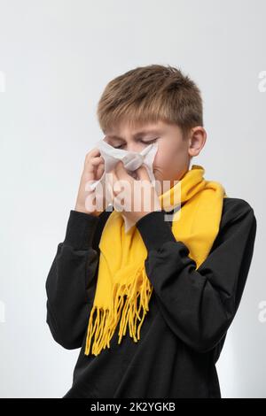 Un enfant souffle son nez dans une serviette, les maladies saisonnières des enfants, un garçon enveloppé dans un foulard, les symptômes de la maladie. Banque D'Images