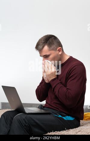 Un homme est mis en quarantaine à la maison pour cause de maladie et travaille en ligne, travaille à distance à la maison, travaille pendant la quarantaine. Banque D'Images