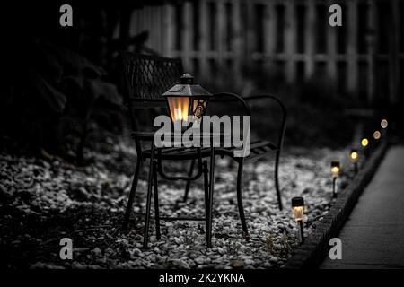 Une échelle de gris d'une lampe de rue sur la chaise métallique noire sur la cour enneigée avec des lampes de jardin autour et un arrière-plan flou Banque D'Images