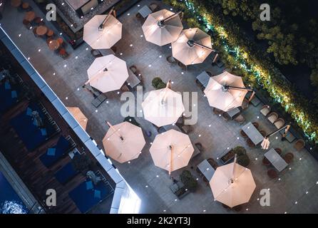 Une vue nocturne sur une esplanade d'un café du complexe ou d'un restaurant avec parasols, tables et chaises, fauteuils inclinables à côté de la piscine, et Banque D'Images