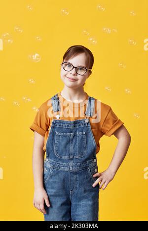 Portrait vertical de la petite fille avec le syndrome de Down regardant l'appareil photo contre fond jaune dans le studio Banque D'Images