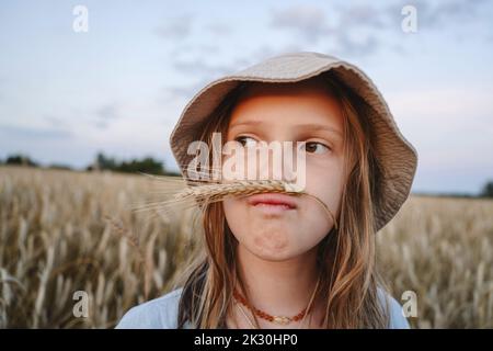 Jolie fille en chapeau faisant de la moustache de maïs de seigle à la ferme Banque D'Images