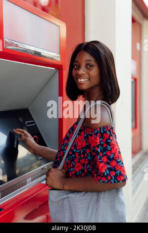 Femme souriante avec un sac à bandoulière à un guichet automatique Banque D'Images