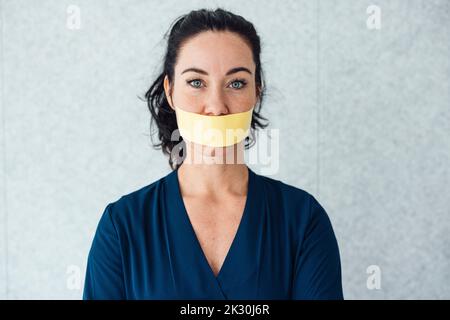 Femme avec du ruban adhésif sur la bouche debout devant le mur gris Banque D'Images