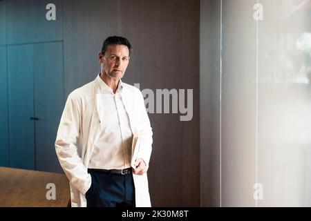 Confident doctor with hand in pocket holding file at hospital Banque D'Images