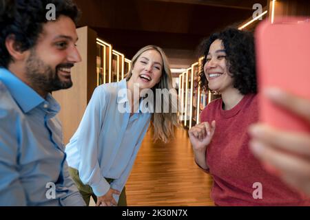 Des collègues multiraciaux rient et prennent le selfie sur un smartphone dans une bibliothèque Banque D'Images
