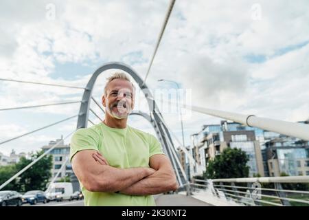 Homme mûr souriant debout sur le pont suspendu de la ville Banque D'Images