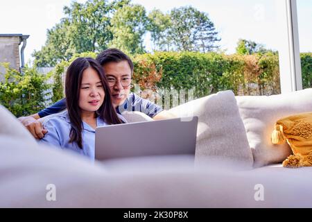 Mature freelancer sharing laptop with man leaning on sofa Stock Photo