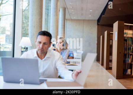 Professeur d'âge mûr travaillant sur un ordinateur portable au bureau dans la bibliothèque Banque D'Images