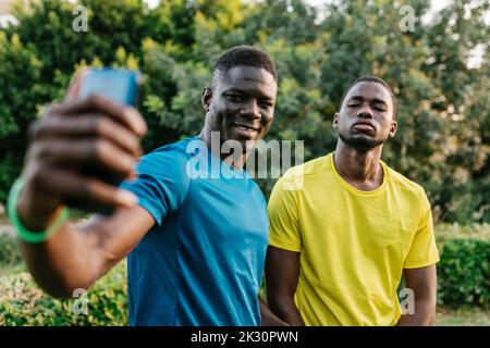 Jeune homme souriant prenant le selfie avec un ami au parc Banque D'Images