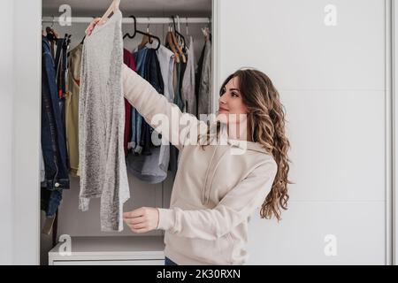 Jeune femme qui cueillez une tenue dans un placard à la maison Banque D'Images
