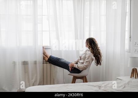 Femme avec de longs cheveux regardant par la fenêtre assis sur une chaise Banque D'Images