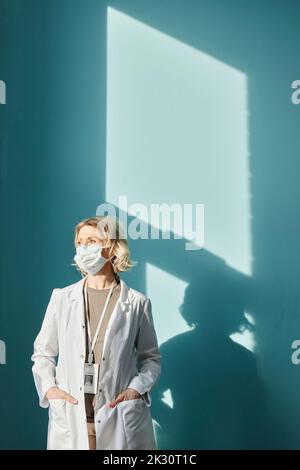 Doctor wearing protective face mask standing in front of wall Stock Photo