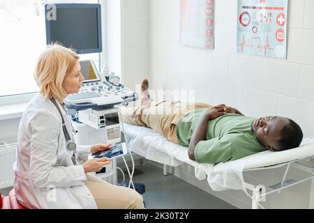 Doctor talking with patient lying on bed doing ultrasound in clinic Stock Photo