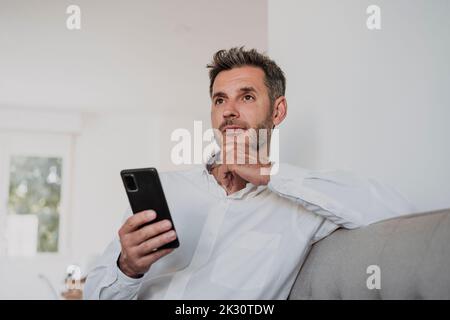 Homme d'affaires attentionné tenant un smartphone sur un canapé dans le bureau Banque D'Images