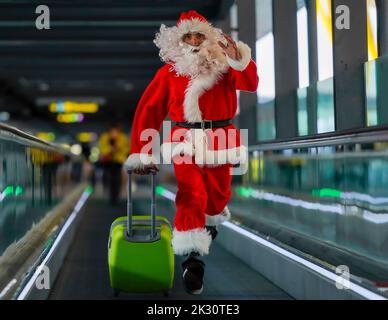 Homme portant le costume du Père Noël et exécutant une valise sur un passage de l'aéroport Banque D'Images