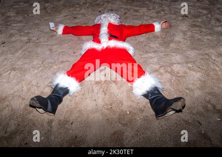 Man wearing Santa Claus costume lying on sand at beach Stock Photo