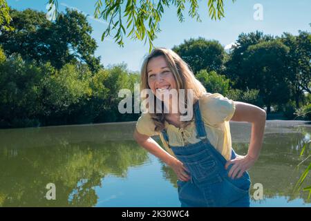 Bonne femme mûre avec les mains sur les hanches debout devant le lac au parc Banque D'Images