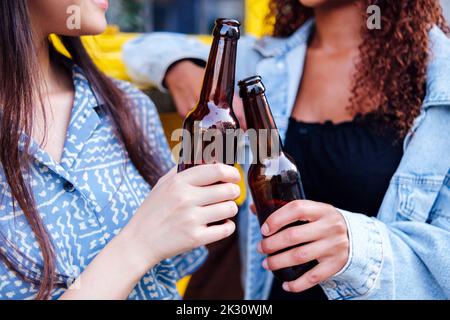 Jeune femme avec un ami pour griller des bouteilles de bière Banque D'Images