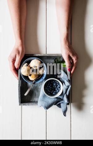 Bras de la femme ramassant plateau avec des bleuets frais et un bol de crème glacée à l'arachide maison Banque D'Images