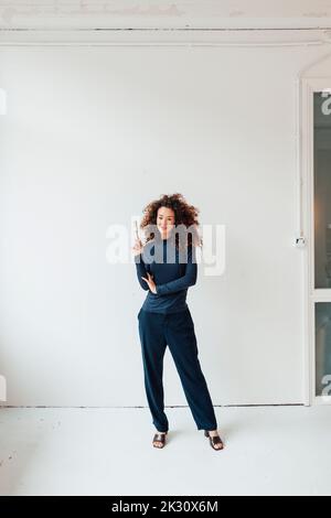 Belle femme avec pinceau debout devant le mur blanc Banque D'Images