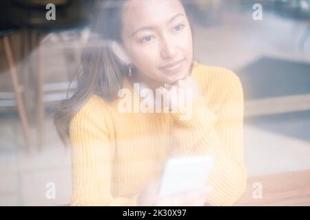 Jeune femme contemplative avec main sur le menton au café Banque D'Images