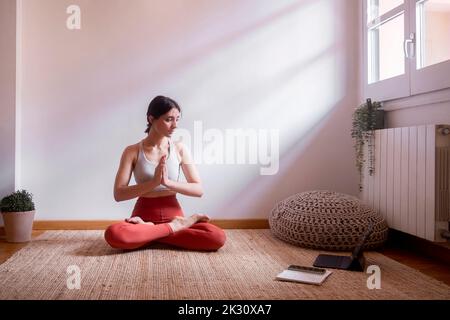 Young woman learning lotus position through tablet PC at home Stock Photo