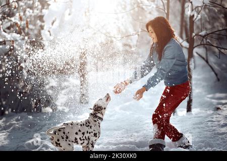 Femme joueur avec un chien dalmatien dans la neige au parc Banque D'Images
