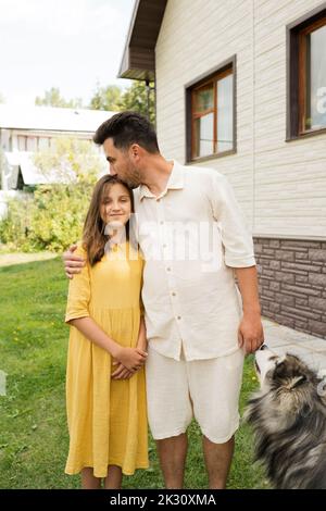 Father kissing smiling daughter by pet dog in back yard Stock Photo