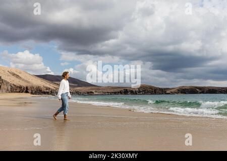 Jeune femme marchant sur le bord de mer à la plage Banque D'Images