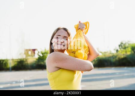 Smiling woman with eyes closed holding lemons in mesh bag Stock Photo