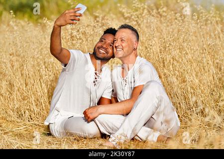 Smiling gay couple taking selfie through smart phone in field Stock Photo