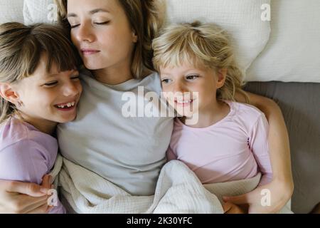 Smiling siblings relaxing with mother in bed at home Banque D'Images