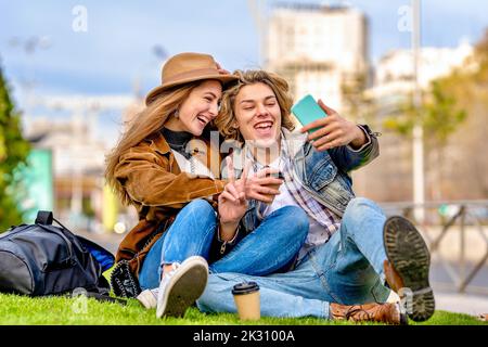 Un couple de touristes heureux qui prend le selfie à travers un téléphone intelligent, assis dans le parc Banque D'Images