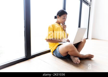 Woman working on laptop leaning against a window Banque D'Images