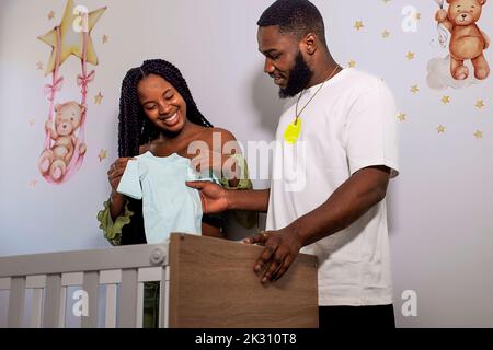 Happy multiracial couple looking at baby clothing Banque D'Images