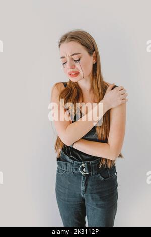 Depressed woman with hand on shoulder crying in front of wall Stock Photo