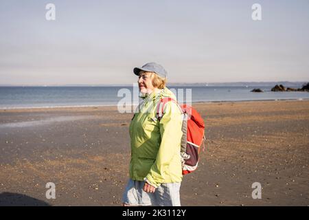 Femme âgée souriante marchant à la plage par beau temps Banque D'Images