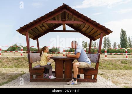 Homme et fille matures mangeant de la nourriture dans une table de pique-nique en bois au parking Banque D'Images