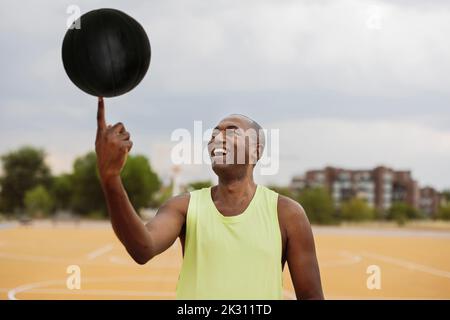 Homme souriant tournant le ballon sur le doigt debout sur le terrain de basket-ball Banque D'Images