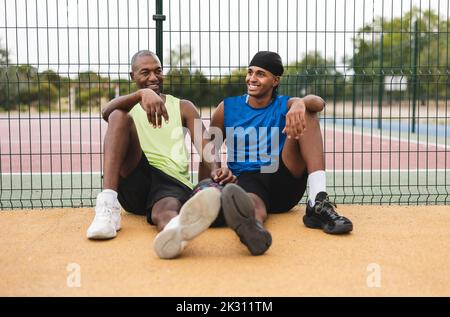 Un fils et un père souriants se penchent sur une clôture, assis sur un terrain de basket-ball Banque D'Images