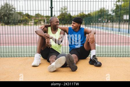 Homme mûr souriant avec son fils assis devant la clôture sur le terrain de sport Banque D'Images