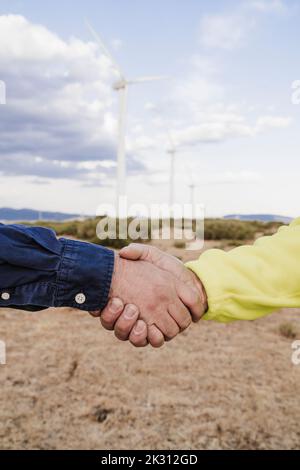 Collègues qui font des poignées de main à la ferme éolienne Banque D'Images