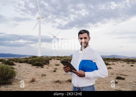 Ingénieur en toute confiance avec un casque qui tient le Tablet PC dans un parc éolien Banque D'Images